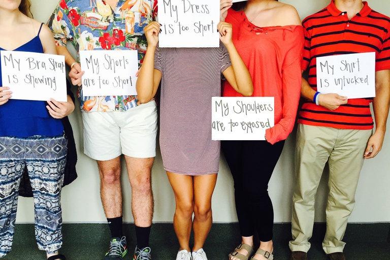 Students+pose+with+signs+stating+their+dress+code+violation.+Students+are+irritated+by+the+strict%2C+unrealistic+dress+code+modifications.+