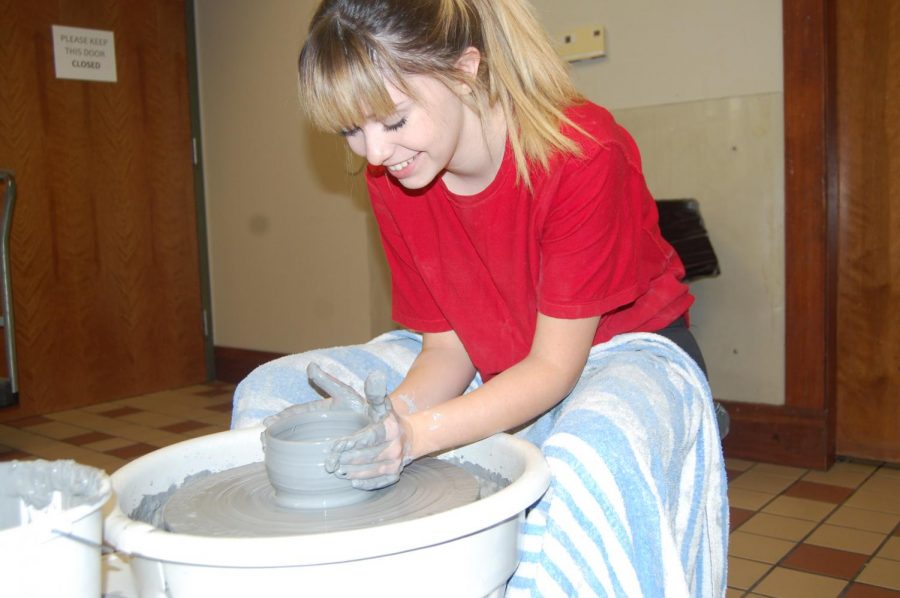 Senior Khai Willis leans over her pottery wheel while shaping a clay bowl. Willis volunteered to do a pottery showcase at the St. Georges Art Show on family day.