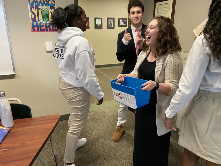 Upper school history teacher Emily Metz laughs as she takes up phones at the beginning of her first period AP Government class. The students are required to put their phones into the blue bin at the start of each class period.