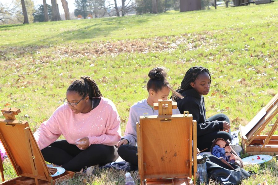 Freshmen Jeniah Moore, Aria Martin and Taylor Christian sit in the grass and paint during morning activities.