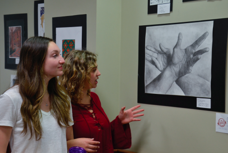 Junior Kate Winstead shows a piece of her artwork to fellow junior Angelina David.