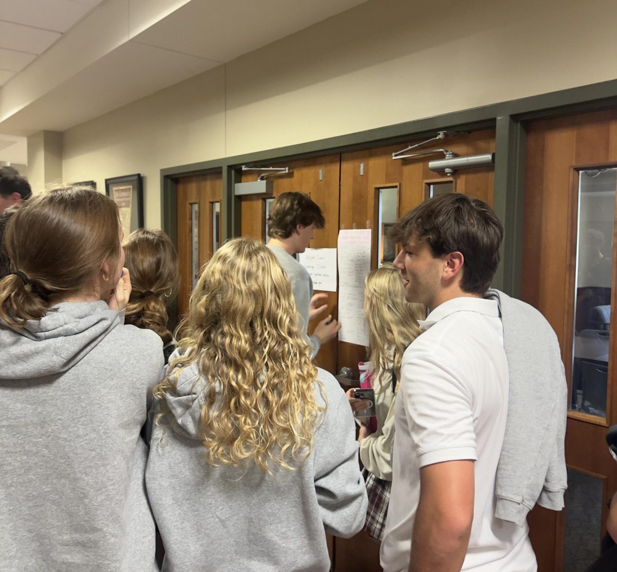 Members of the Class of 2026 huddle around the entrance to the upper school lounge as Hudson Burns signs the pledge. 